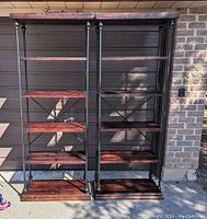 Pair of wood and metal display stands photographed outdoors against a brick wall, showing full front view.