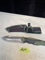 Photo of knife with sheath, blade exposed showing curved tip and gut hook, handle in black and green with textured grip