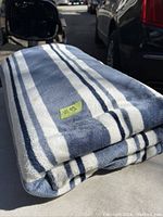 Folded large blanket with blue and white stripes laid out on a surface, visible texture and pattern.