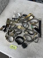 Photo showing a collection of approximately 21 wristwatches in mixed metal finishes and styles laid out on a white surface.