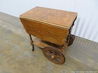 Side view of walnut drop leaf tea wagon showing drawer, swing handle, turned legs, lower shelf, and wood grain finish.