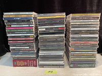Three stacks of assorted music CDs showing titles and artists such as U2, Jay-Z, Shania Twain, Eric Clapton, AC/DC, The Doors, Talib Kweli, and more.