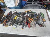 Overview of assorted hand tools and power tools arranged on a table showing various pliers, adjustable wrenches, screwdrivers, and several cordless drills.