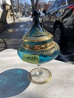 Photo showing a blue tinted glass jar on a pedestal foot with lid and gold ornamental accents.
