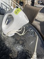 Side view of the white electric hand mixer with attached beaters and power cord, showing its overall shape and condition.