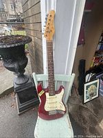 Front view of red Jay Turser electric guitar resting on a chair, showing full body and neck.