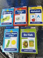 Photo showing five sets of kids learning flash cards and game cards from Baby Fun brand lying on a blue surface. The decks include Sight Words, Numbers 0-25, Alphabet, Colors, Shapes & More, and Go Fish cards with animal illustrations.