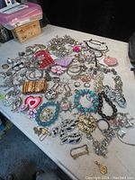 Wide view of assorted estate costume jewelry items on table with chains, earrings, brooches, bracelets and rings.