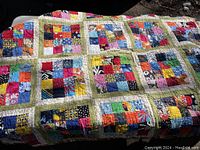 Full view of colorful patchwork quilt spread out, showing multicolored small square patches sewn together with light green borders.