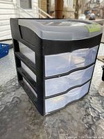 Side and front view of the black plastic storage unit with three clear drawers and a hinged lid on top.
