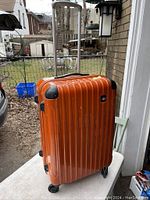 View of orange hard shell suitcase standing upright showing its vertical ridged design and extendable handle.