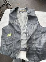 Black vintage leather vest laid flat on a surface, showing front side with lining and brand tag 'Geronimo'.