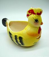 Side angle showing yellow ceramic hen egg separator with red and black paint accents and open cavity for separating eggs