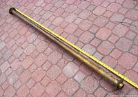 Full length view of the brass bar rail placed on a paved surface with measuring tape along its length showing about 76 inches.
