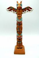 Full front view of wooden totem pole with colorful painted carved figures including bird with outstretched wings on top.