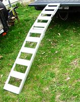 Full view of the lightweight aluminum folding ramp extended from a vehicle, set on the ground with grassy area below.