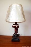 Table lamp with a white lampshade covered in plastic and a fishing motor inspired base on a wooden surface against a light wall.