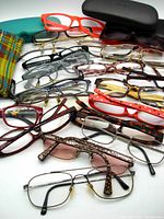 Various reading glasses in assorted frame styles and colors along with glasses cases displayed together