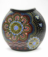 Front view of rounded black vase with large central ring dot pattern in red, white, blue and yellow representing Australian Aboriginal star symbols.