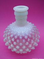 Front and side view of the vintage Fenton hobnail opalescent glass vase showing the rounded hobnail design, opalescent white to pale pink glass and ribbed neck on a bright pink background.