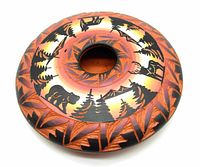 Top angled view of red clay seed pot showing painted black silhouettes of animals and trees with geometric carvings and southwestern color gradient