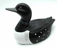 Front side view of the ceramic loon coin bank showing the black body, white chest, dotted wings, and red eye.
