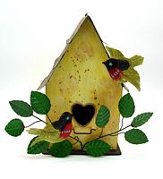 Front view of yellow painted tin bird house decorated with two red-breasted robins perched on metal branches with green leaves, heart-shaped entrance hole visible.