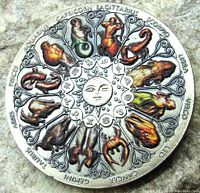 Photo showing front view of a round metal zodiac token with detailed colorful astrological sign artwork arranged around a central sun face.