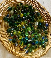 Wicker platter filled with over 100 vintage spiral glass catseye marbles in varied colors and spiral patterns.