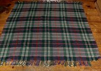 Top view of the tartan patterned wool blanket laid flat on wooden surface showing the full design and tassels on one end.