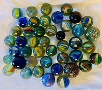 Top view showing approximately 40 large glass shooter marbles in assorted colors and swirl patterns on white background.