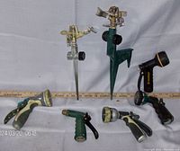 Image showing two lawn sprinklers with spikes and five assorted hose spray nozzles arranged in front of a white background with measuring stick behind.