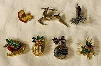 Seven holiday brooches in a row on light surface, showing entire lot.