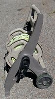 Garden hose wound on beige plastic hose reel cart, side view showing wheels and structure.