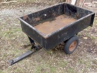 Full view of black steel garden trailer with flat rectangular bed and two wheels, showing rust and dirt.