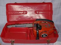 Orange Homelite XL chainsaw inside red plastic carrying case with 14-inch Husqvarna guide bar and chain visible