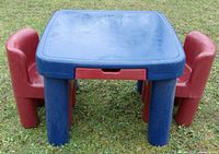 Front view of blue table with two red chairs at left and right sides on grass.