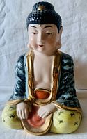 Front view of the vintage ceramic Buddha statue showing meditative pose, detailed facial features, and colorful glazed robe and pants.
