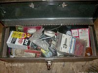 Metal tool box open showing assorted hardware including boxes of connectors, clamps, screwdriver bits, sockets, and wrenches inside.