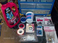 Lot displayed on workbench showing red bottle of Drano Max Gel, white container of plumber's putty, multiple rolls of plumber’s tape in white, yellow, red and black colors, and packs of Master Plumber O-rings and fittings.