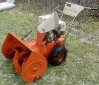 Side view of orange and white Allis-Chalmers Tracker 8 snowblower showing auger, chute, wheels with chains and Briggs engine.
