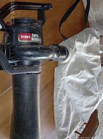 Black Toro Super Blower Vac handheld leaf blower vacuum showing side label and attached white fabric leaf collection bag.