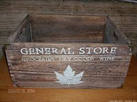 Front view of wooden box showing 'GENERAL STORE' text, maple leaf design, and rustic weathered finish.