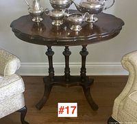Full view of walnut parlour table showing scalloped top with silver tea set on top and upholstered chairs flanking.