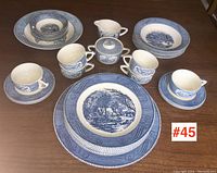 Full set of six place settings with cups, saucers, plates, bowls, plus cream and sugar set arranged on table.