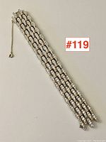 Full length view of the multi-row silver-tone bracelet laid flat, showing the safety chain and clasp, placed on a plain background.