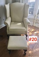 Wing-back chair and matching footstool positioned on hardwood floor near window, showing full front view of both pieces.