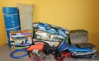 Full lot contents showing a green Coleman 8-person Sundome tent carry bag, blue and gray rolled tarps, a beige tent bag, orange hand pump, headlamps, blue tubing, battery box, and boxed queen size travel mattress.