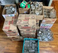 Overall lot of mason jars including Bernardin boxed jars, loose jars, and lids in containers, displayed on floor