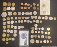 Overview of the mixed international coin collection spread on a dark surface showing multiple rows of coins including a New Hampshire State Quarter in sealed packaging.